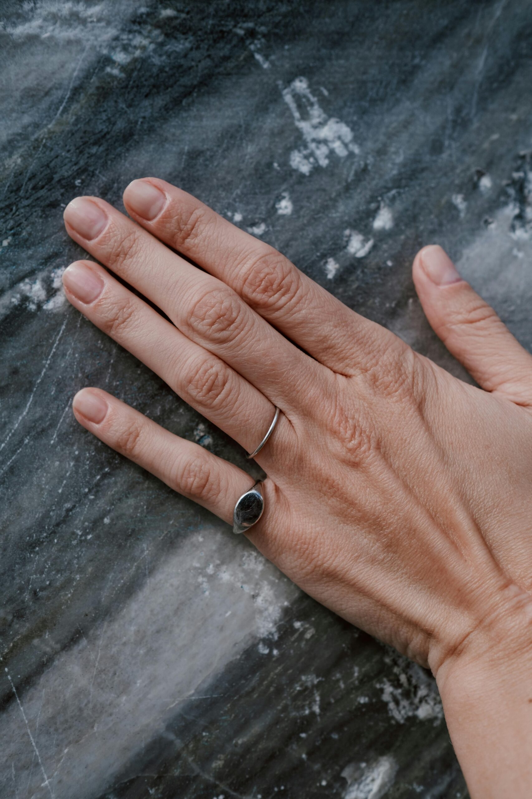 A woman's hand adorned with rings resting on a textured marble surface.
